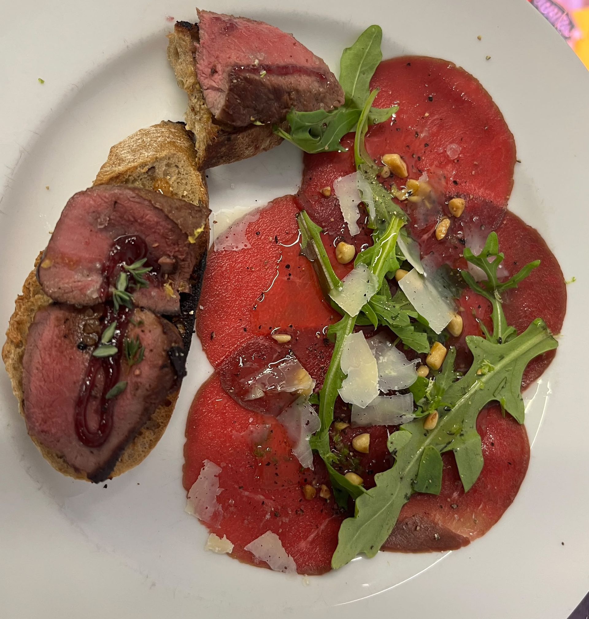 Auf einem Teller angerichtete Rindfleischscheiben mit Rucola und Rote-Bete-Carpaccio, garniert mit Kräutern und Sauce