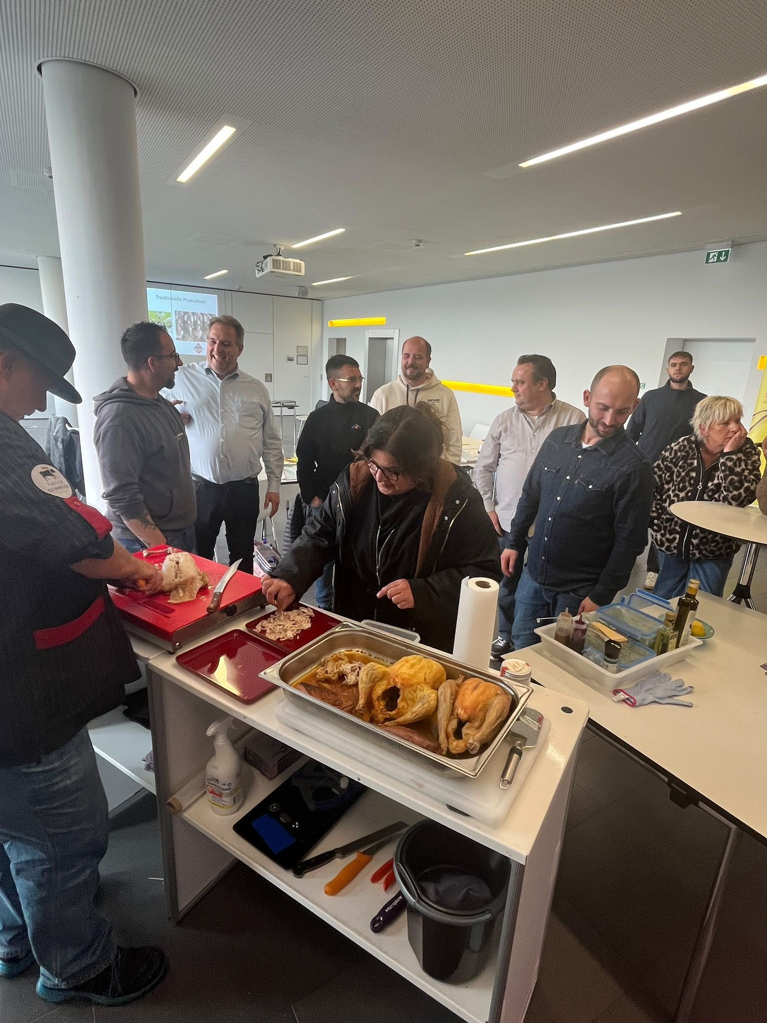 Menschen stehen in einem hellen Aufenthaltsraum im Büro um ein Buffet und bedienen sich am Essen, während sie sich unterhalten.