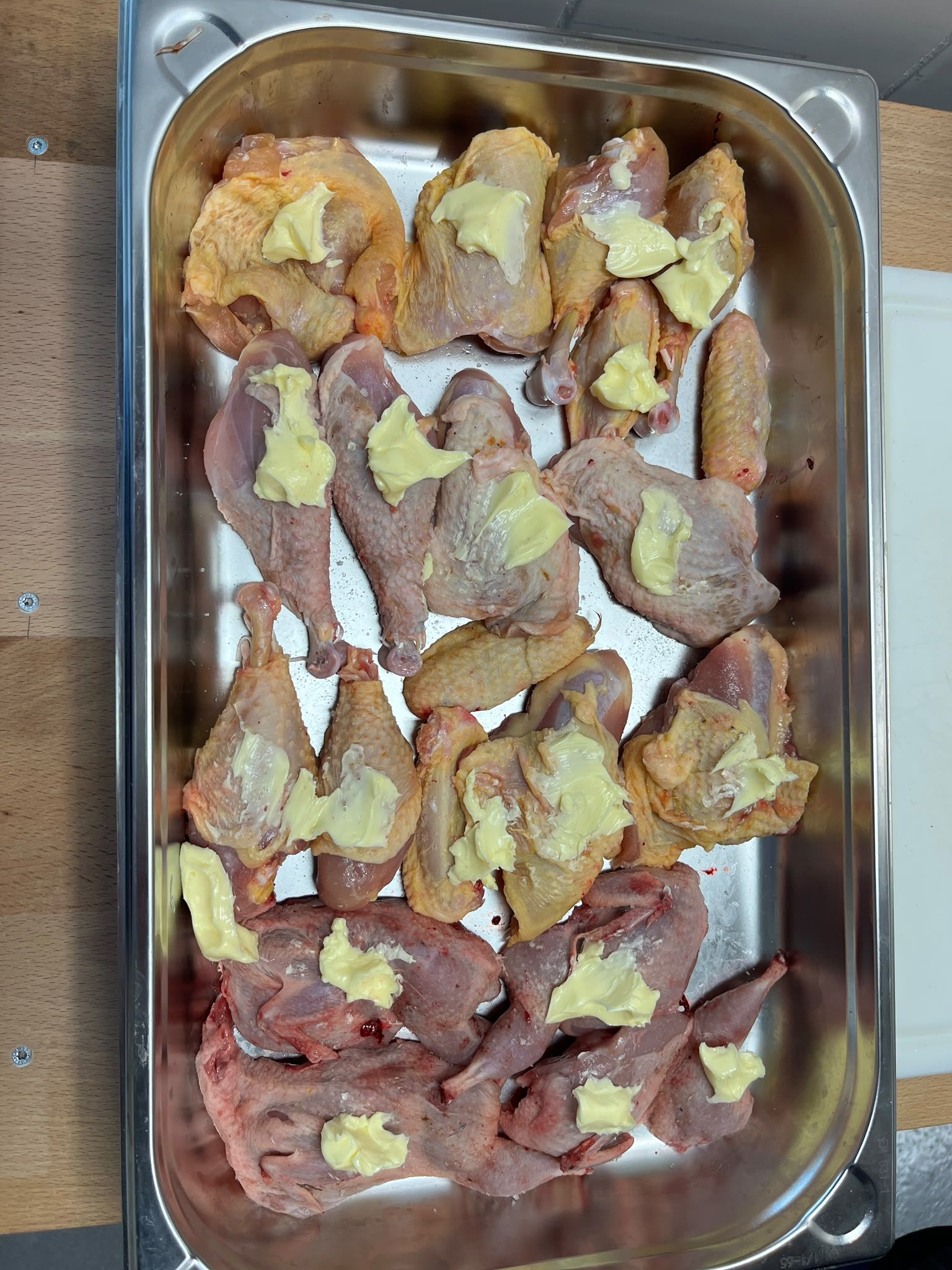 Auf einem Metallblech angerichtete rohe Hähnchenteile, bedeckt mit blassgelber Butter oder Gewürzmischung.