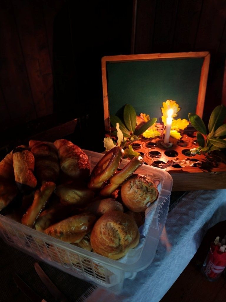 Korb mit verschiedenen Brötchen und Gebäck neben einem kerzenbeleuchteten Brett in einem dämmrigen Raum