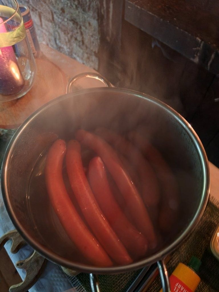 Mehrere Hotdogs köcheln in einem dampfenden Topf auf dem Herd