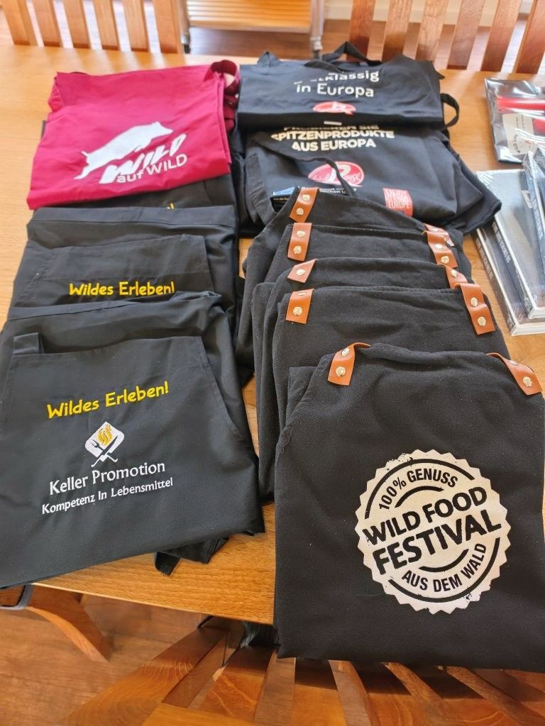 Schwarze und rote T-Shirts mit Logo liegen auf einem Holztisch bei einem Wildpflanzen-Festival.