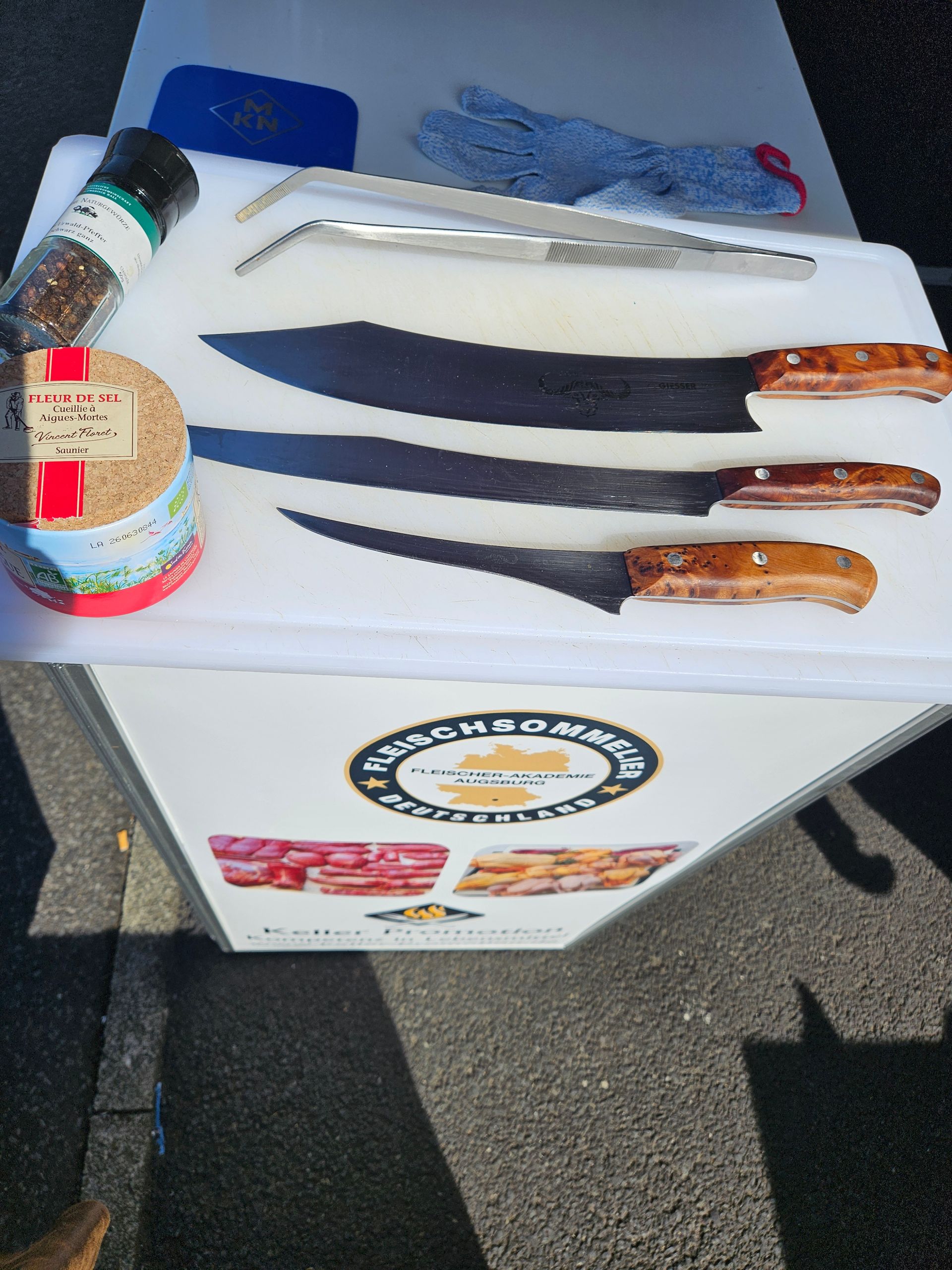 Drei Messer und eine Flasche Gewürzmischung auf einer weißen Kühlbox im Freien
