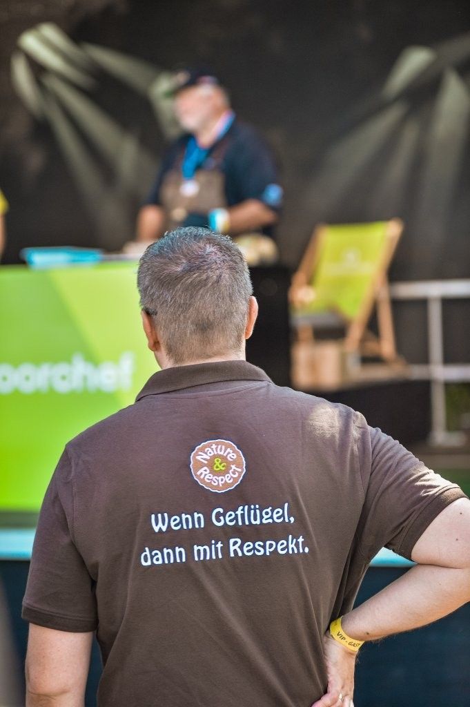 Person in dark polo watching a stage performance; shirt reads “Wenn Gefällt, dann mit Respekt.”