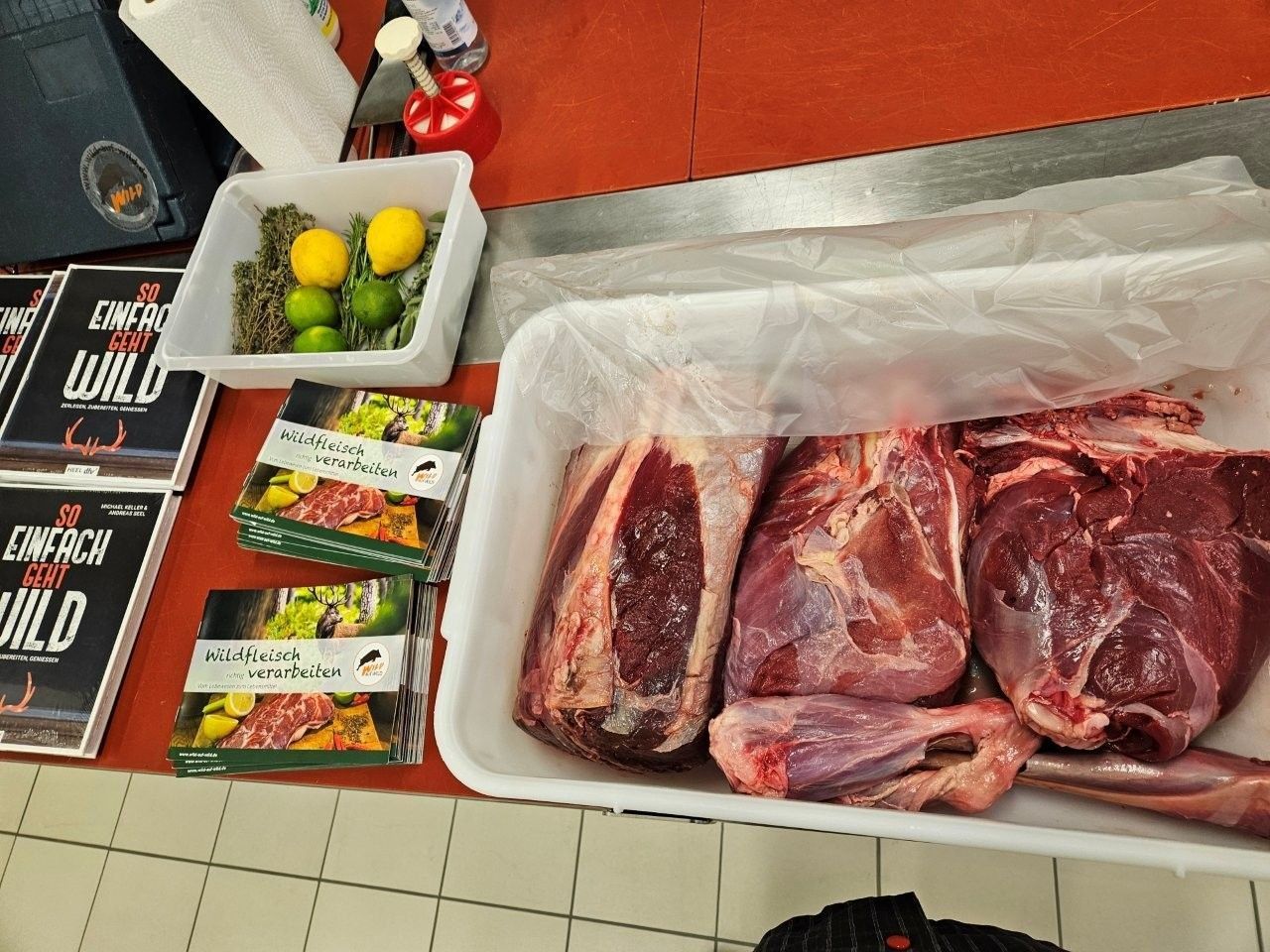 Fleisch in Kiste. Daneben Schale mit Zitronen und Gewürzen und einem Buch