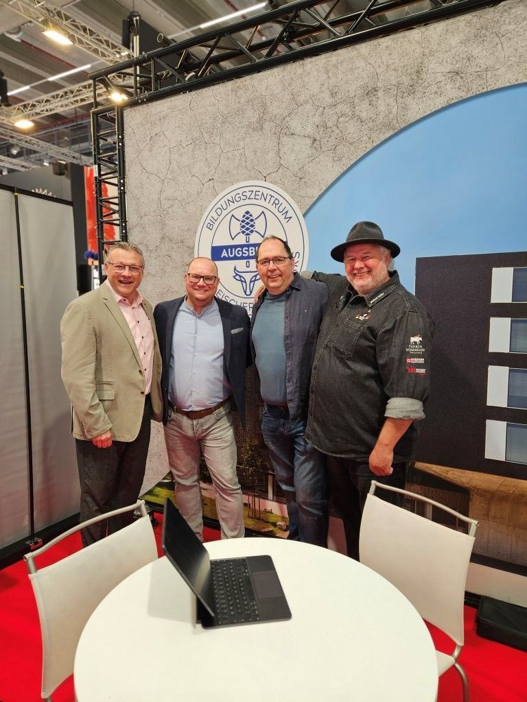 A group of men are standing around a table with a laptop on it.