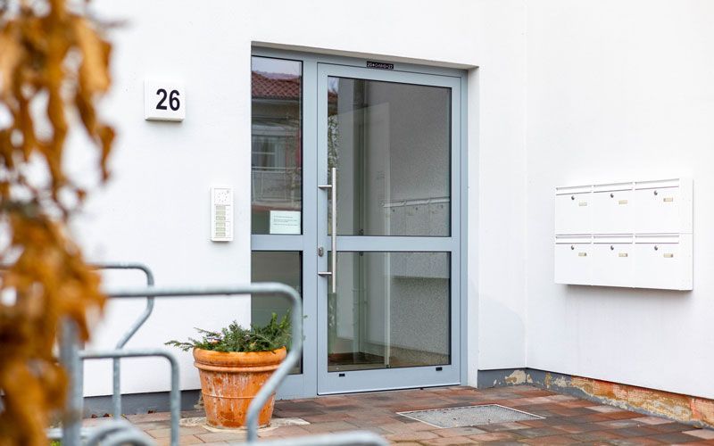 Ein weißes Gebäude mit einer Glastür und einer Topfpflanze davor.