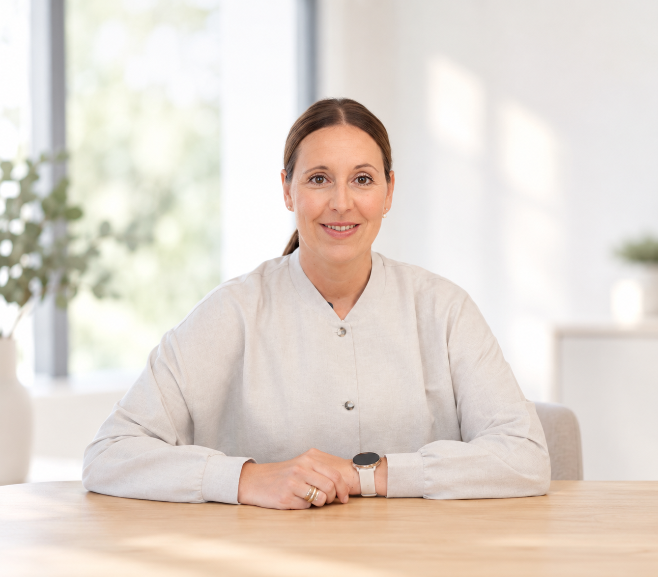 Eine Frau sitzt in einem modernen Büro an einem Tisch mit Büchern und lächelt in die Kamera.
