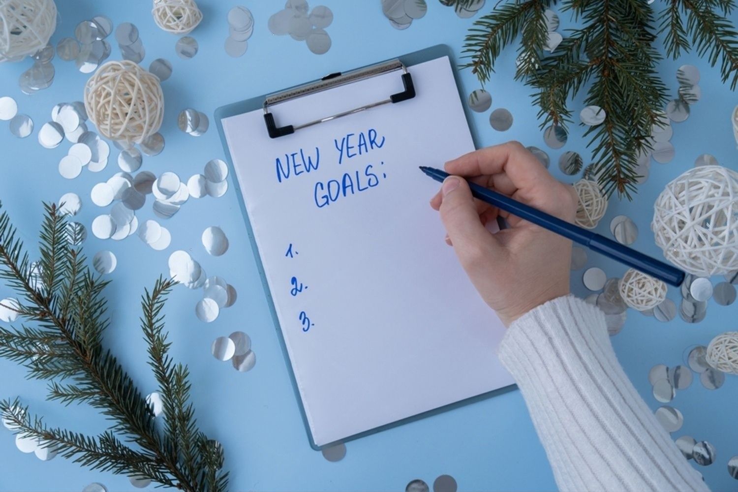 Klemmbrett mit To-do-Liste auf blauem Hintergrund, während eine Hand Notizen schreibt.