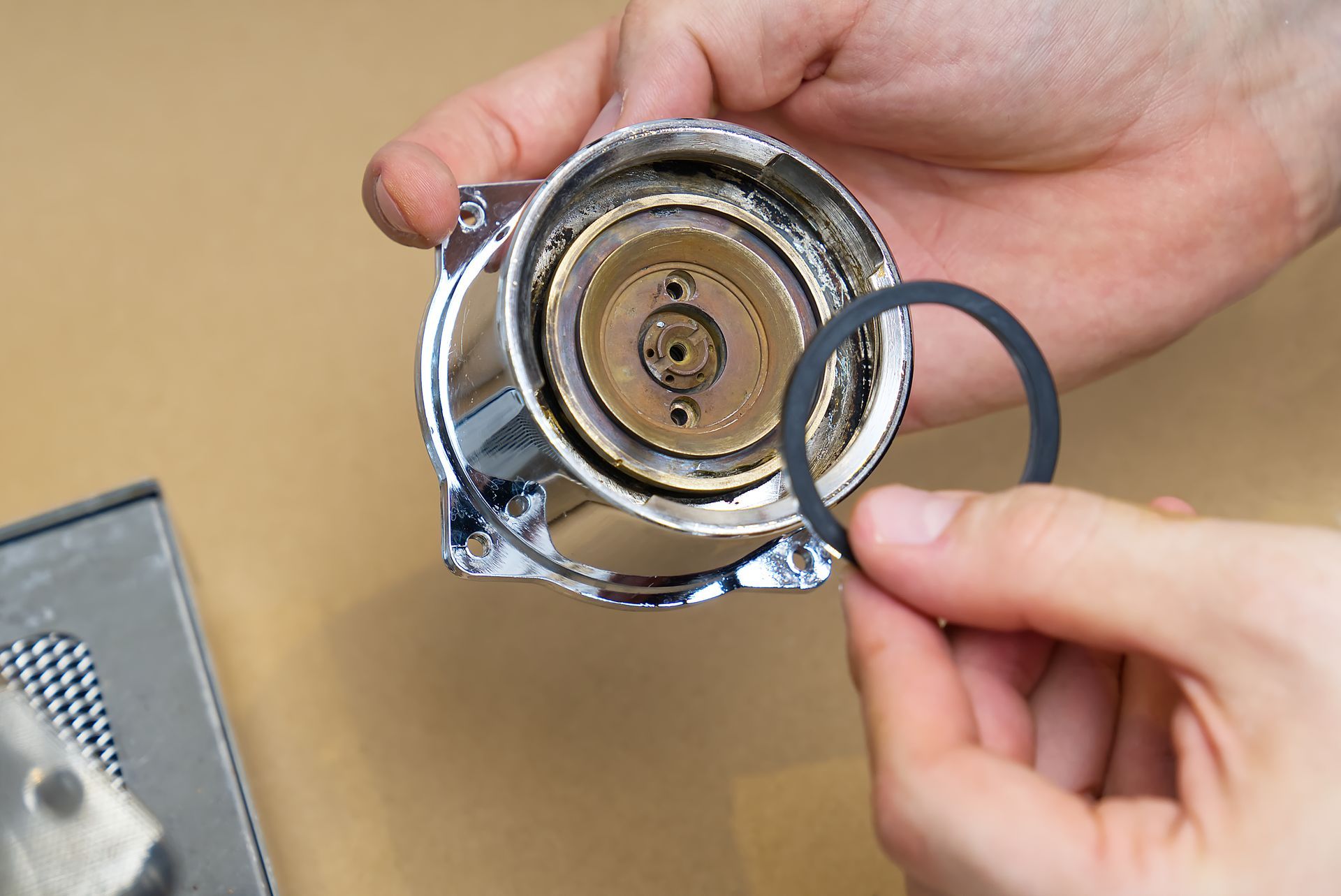 Des mains tenant un joint torique en caoutchouc noir près d'une pièce chromée démontée d'une machine à expresso.
