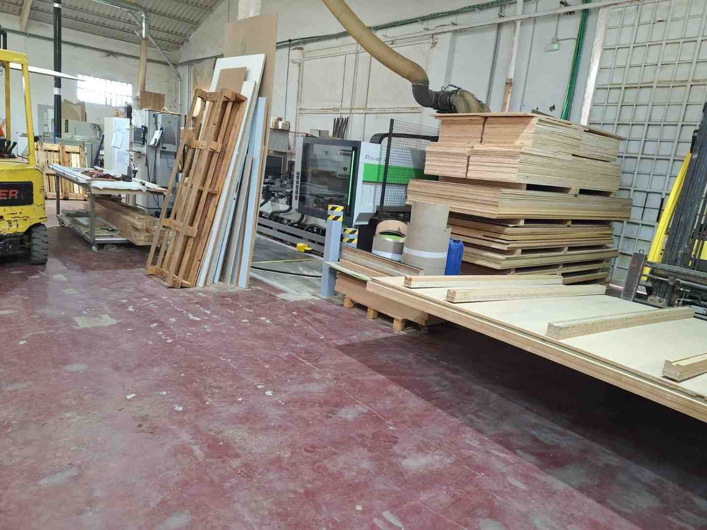Taller de carpintería con pilas de madera contrachapada, estanterías para madera y herramientas.
