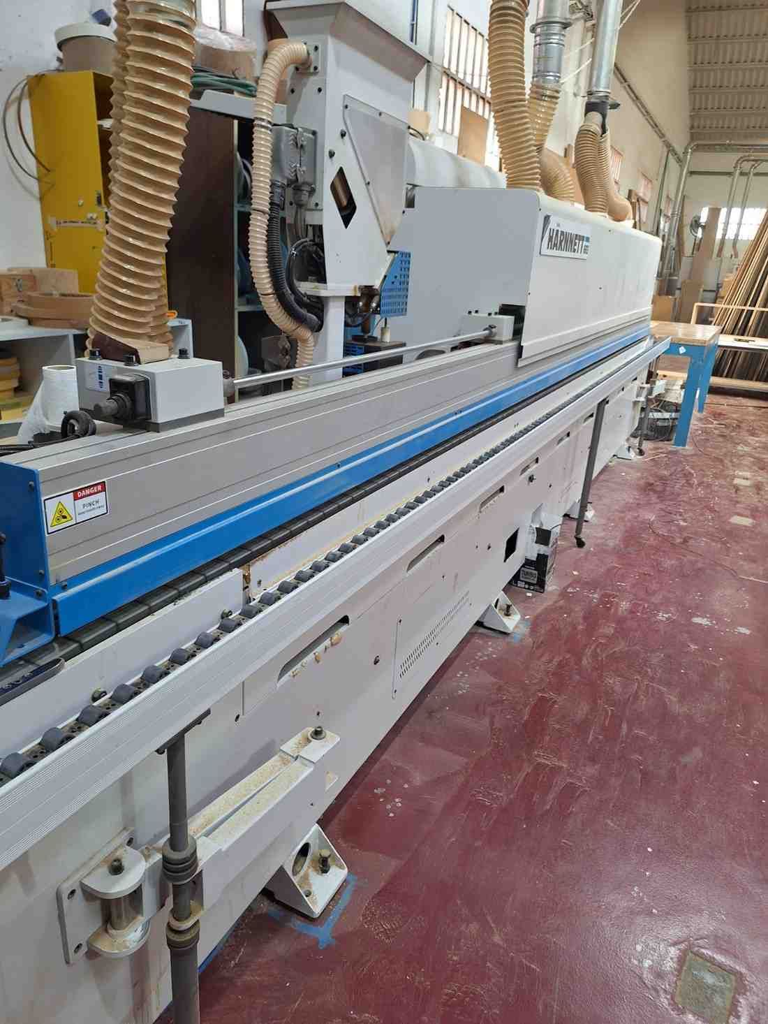 Máquina industrial larga en un taller con raíles azules y paneles blancos sobre un suelo rojo.