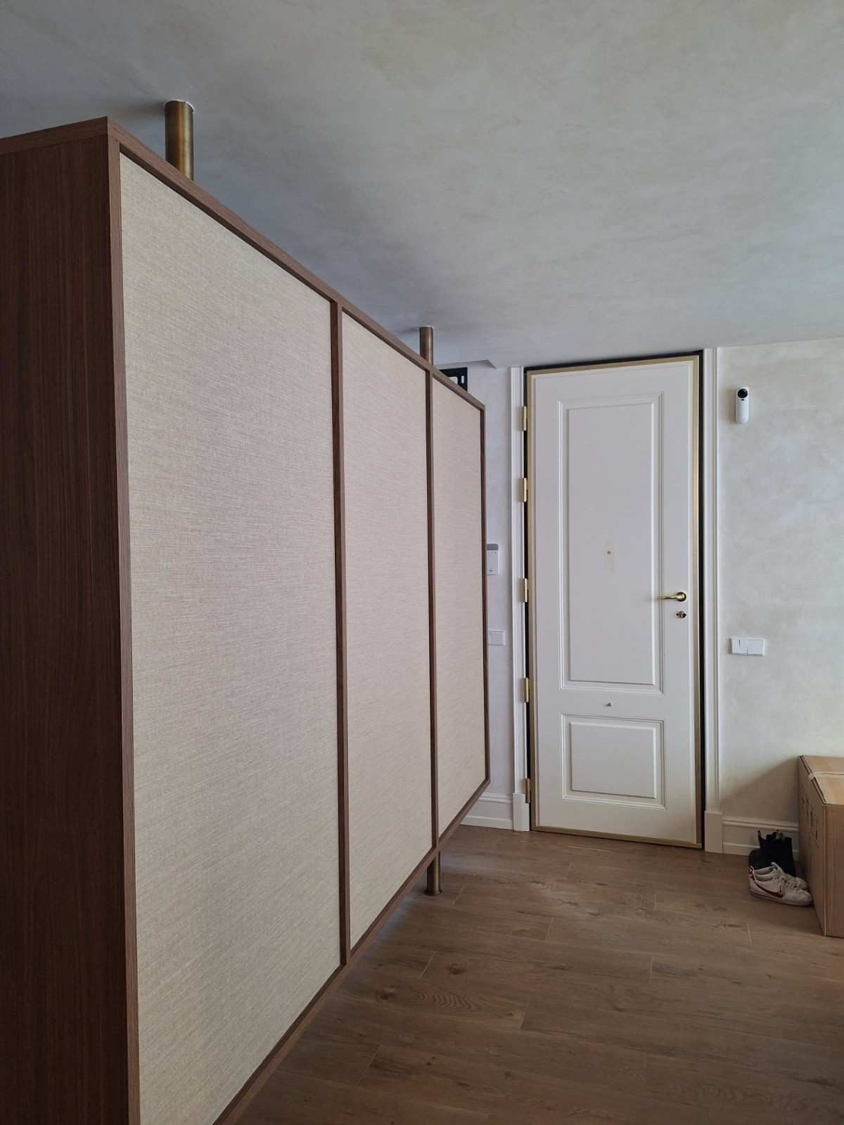 Pasillo estrecho con grandes tabiques beige, puerta blanca y cajas de cartón a la derecha.