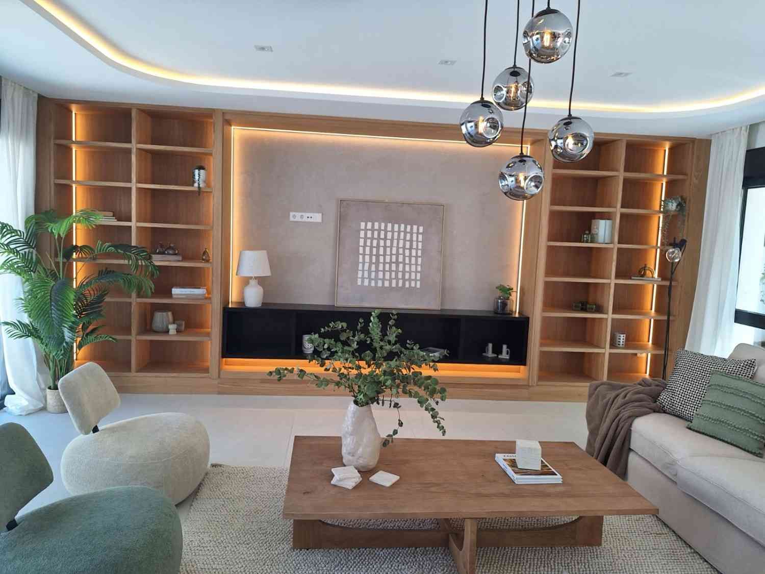 Sala de estar moderna con estanterías de madera empotradas, sofá blanco, mesa de centro y lámparas colgantes.