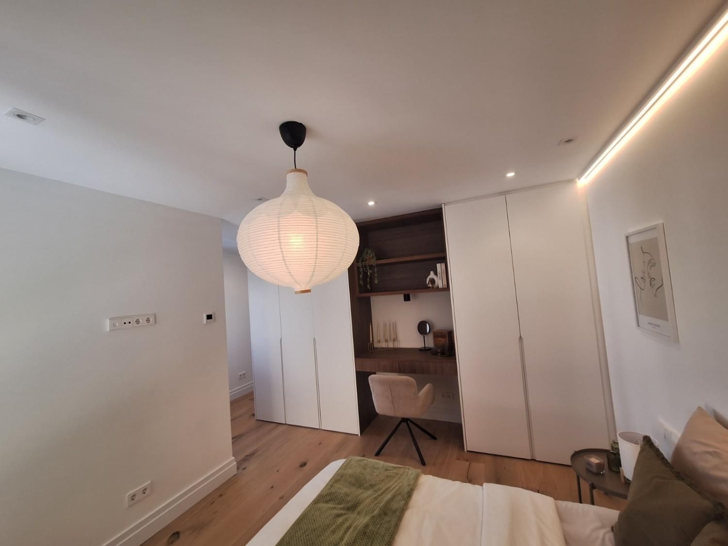 Sala de estar luminosa con una linterna de papel colgante, paredes blancas, suelo de madera.