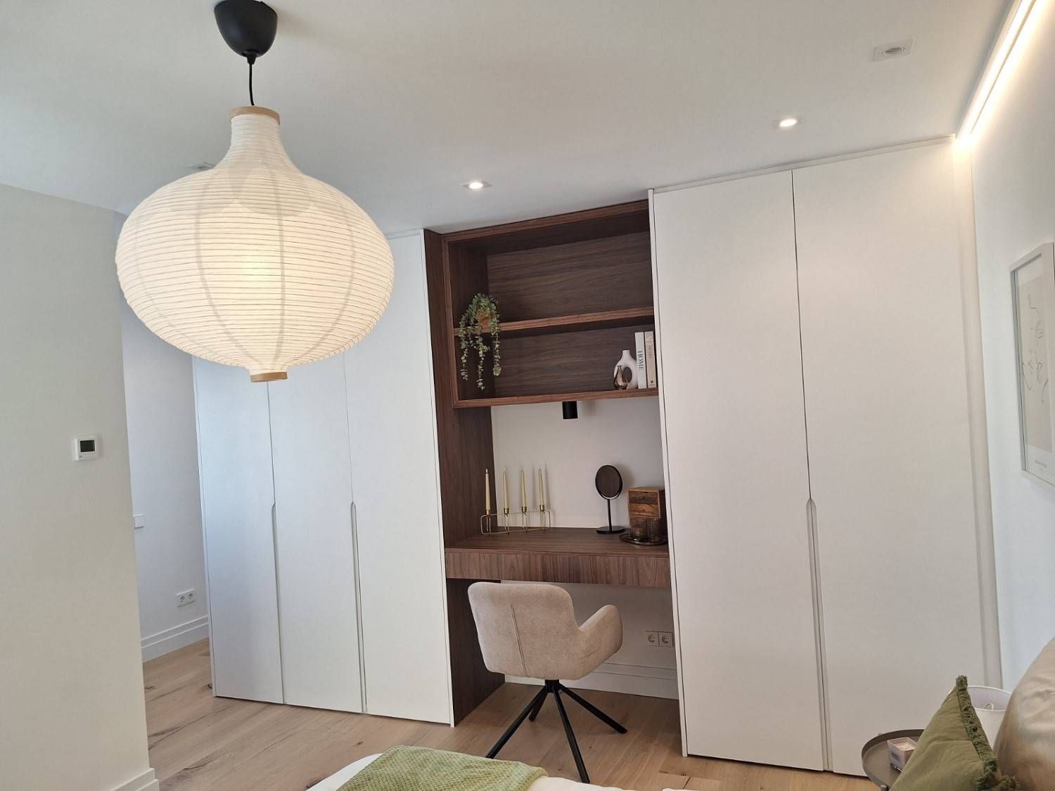 Despacho luminoso y minimalista con armarios empotrados blancos, rincón de escritorio de madera, silla y lámpara.