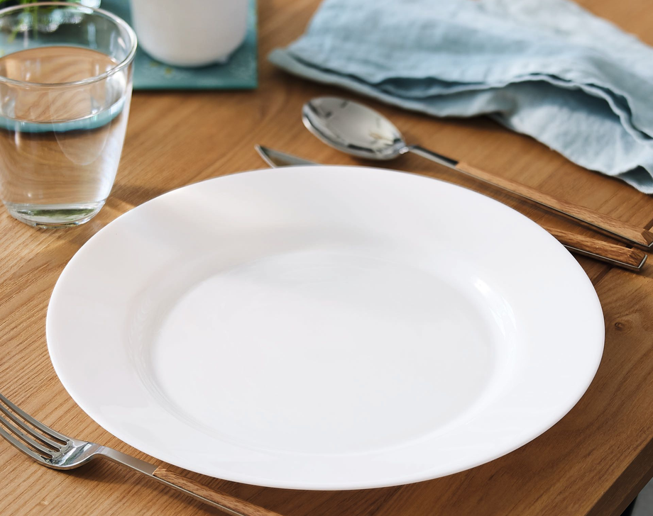 Assiette blanche sur table avec couverts et un gobelet