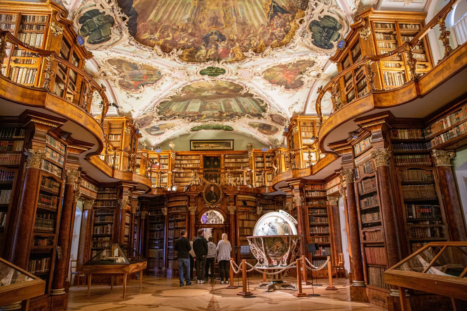 Der eindrucksvolle Barocksaal der Stiftsbibliothek St. Gallen mit reich verzierten Deckenfresken, historischen Holzregalen, tausenden antiken Büchern & einem kunstvollen Globus im Mittelpunkt.