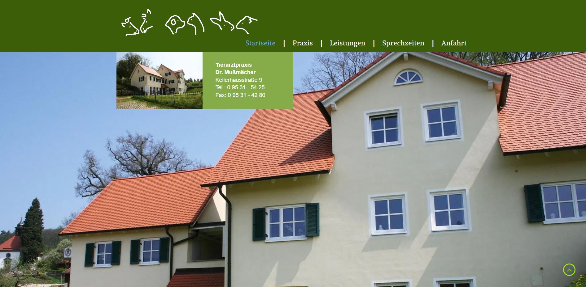 Beiges Gebäude mit rotem Ziegeldach und grünen Fensterläden unter einem klaren blauen Himmel.