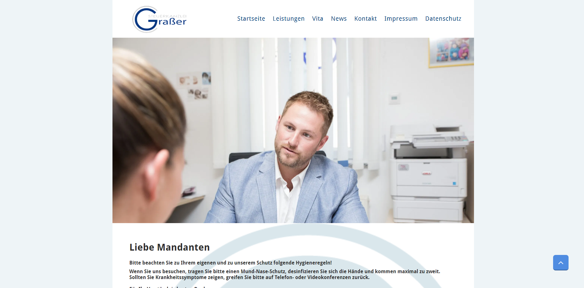 Ein Mann in einem blauen Blazer sieht in einer Büroumgebung jemanden außerhalb des Bildes an.