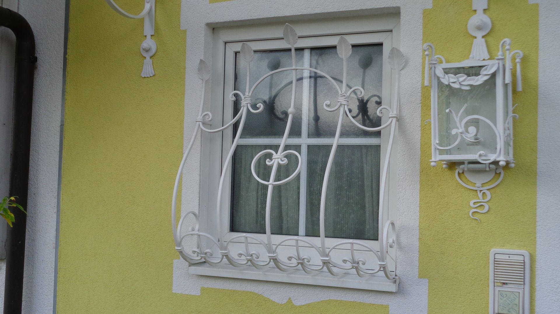 Weißes Fenstergitter mit geschwungenen Verzierungen vor Fenster