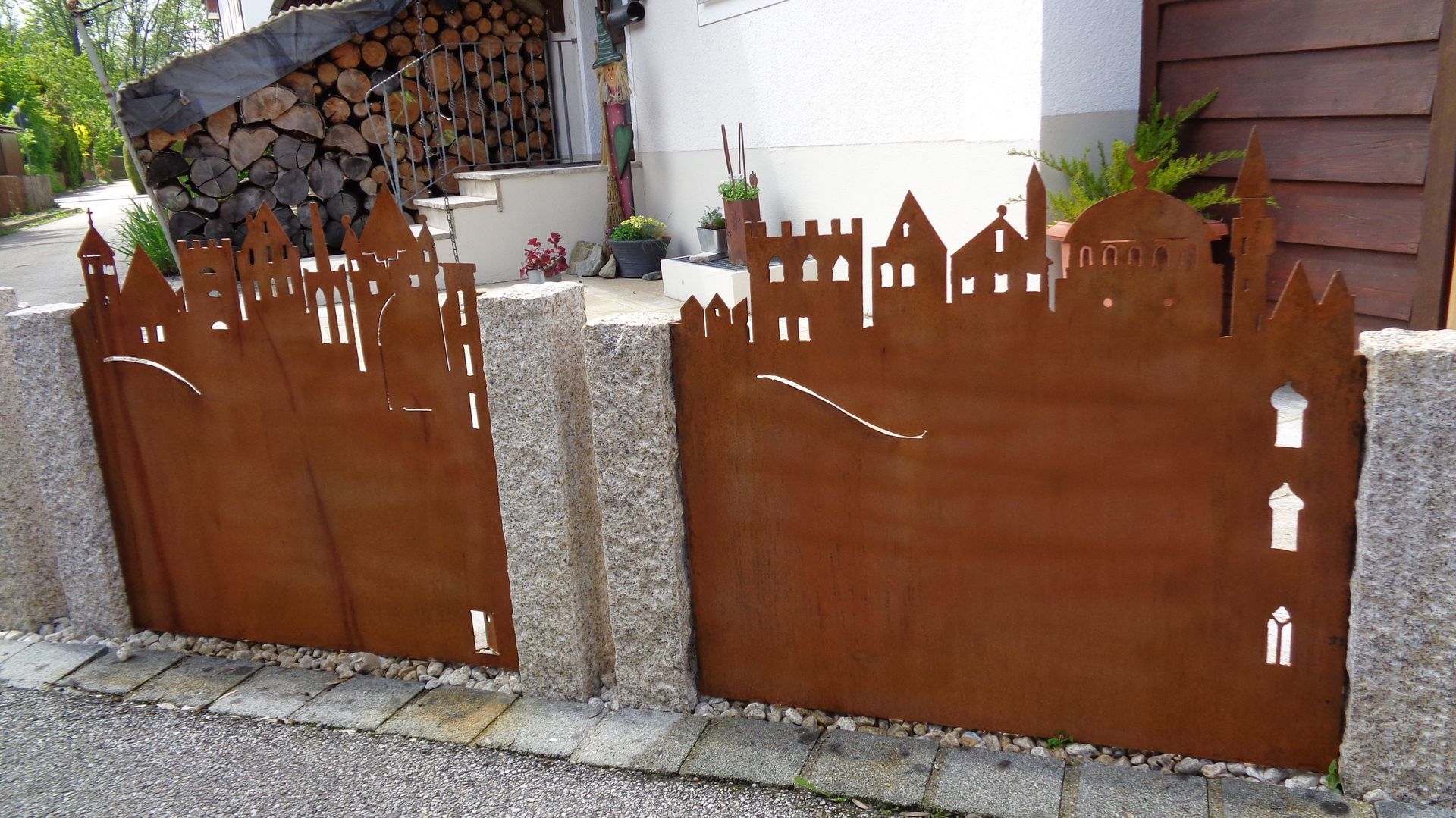 Rostfarbene Metall-Gartentür mit Stadtsilhouetten-Motiv neben Hauswand