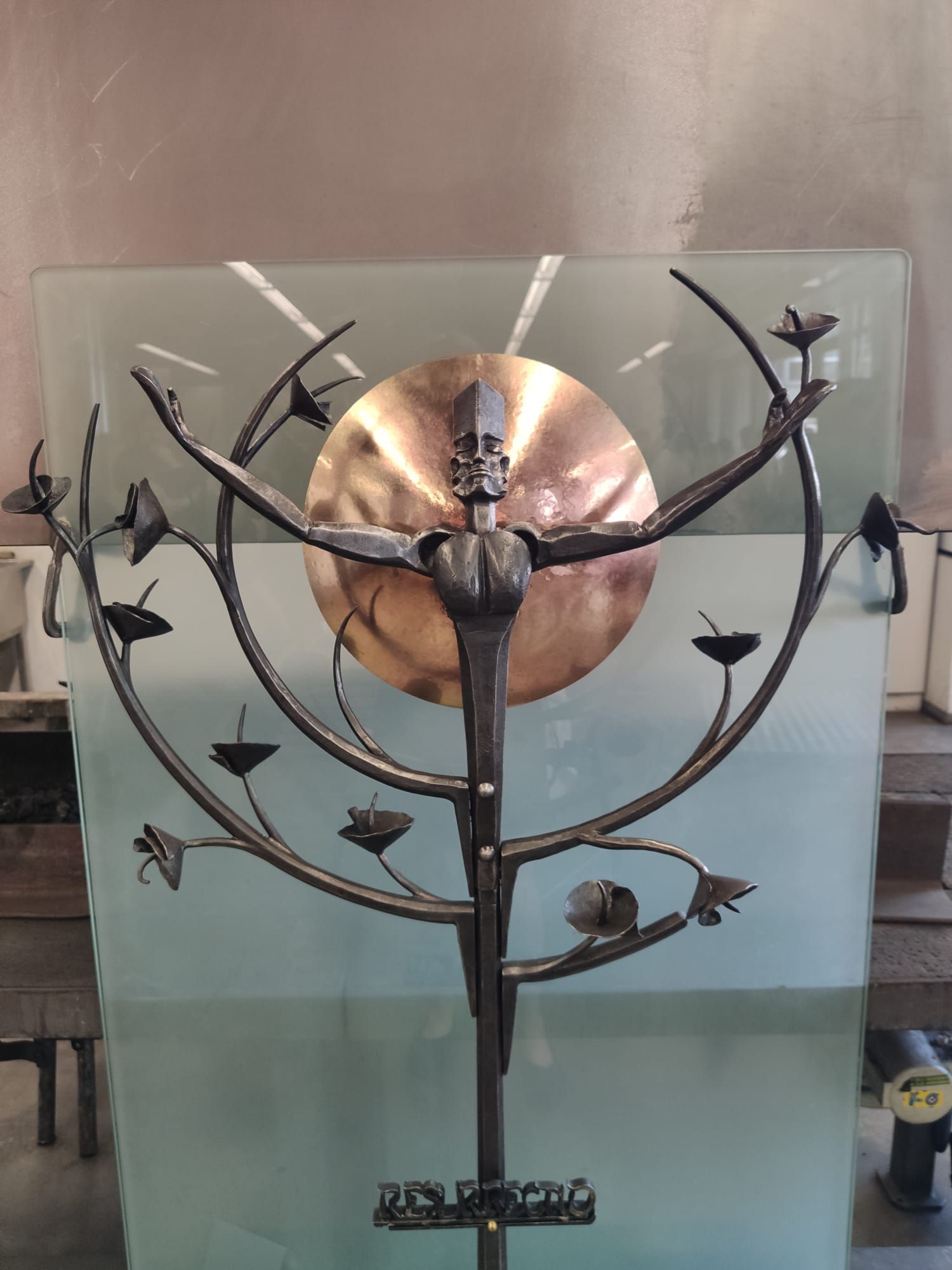 Metallskulptur mit menschlicher Figur vor runder Scheibe