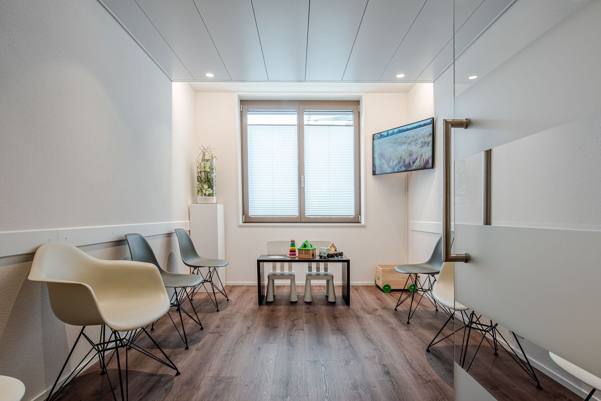 Ein Wartezimmer mit einem Tisch und Stühlen und einem Fernseher an der Wand.