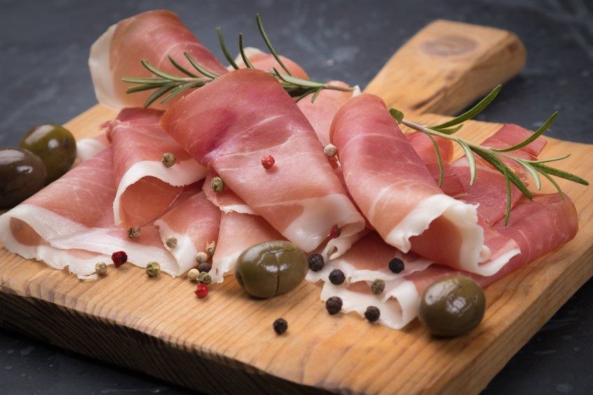 Lonchas de jamón y aceitunas sobre una tabla de cortar de madera.