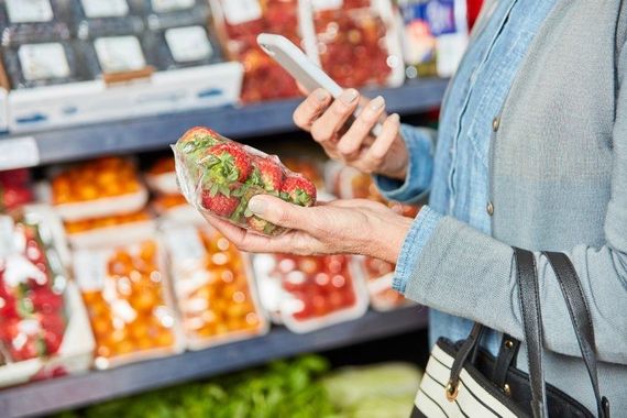 Una mujer sostiene fresas y usa un teléfono celular en una tienda de comestibles.