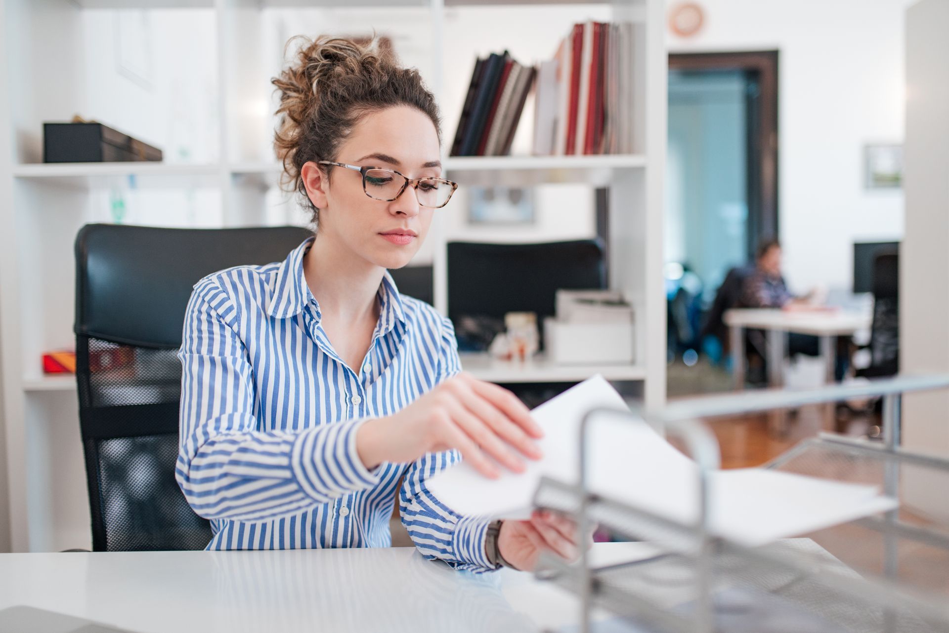 Image d'une femme assise devant un bureau tenant des feuilles de papier dans les mains
