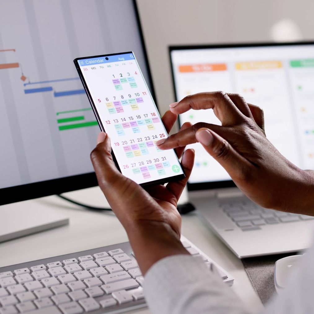Image d'un agenda électronique sur un smartphone et des écrans d'ordinateur avec des plannings en arrière-plan
