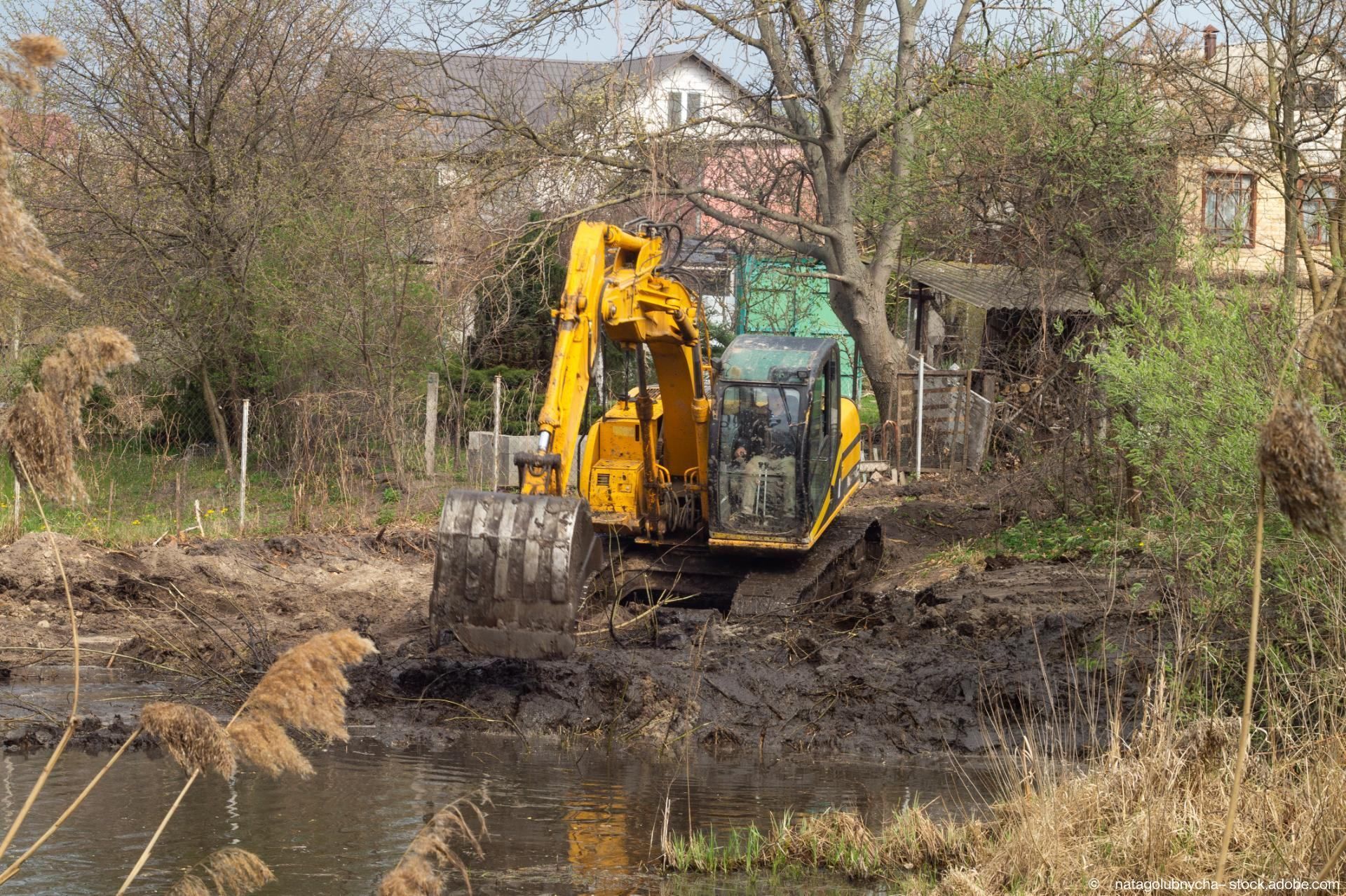 Ein Bagger schaufelt etwas an einem See