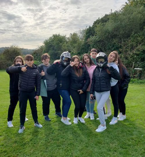 Un grupo de personas vestidas de manera informal posan al aire libre, algunas de ellas llevan cascos de motocicleta.