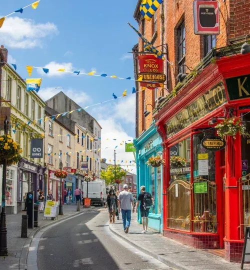 Calle llena de tiendas y edificios coloridos en una ciudad europea, gente caminando.