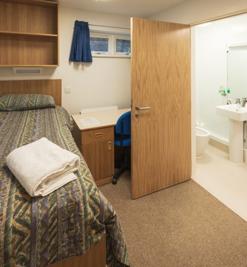 Una habitación compartida con una cama, un escritorio y una puerta de baño que se abre para mostrar un lavabo.