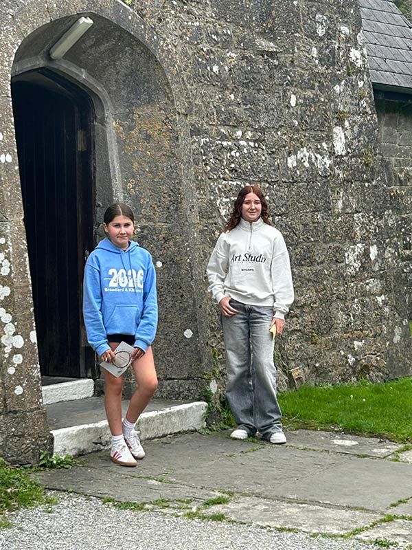 Dos personas posando junto a la puerta de un edificio de piedra, una con una sudadera azul con capucha y la otra con una sudadera gris con capucha.