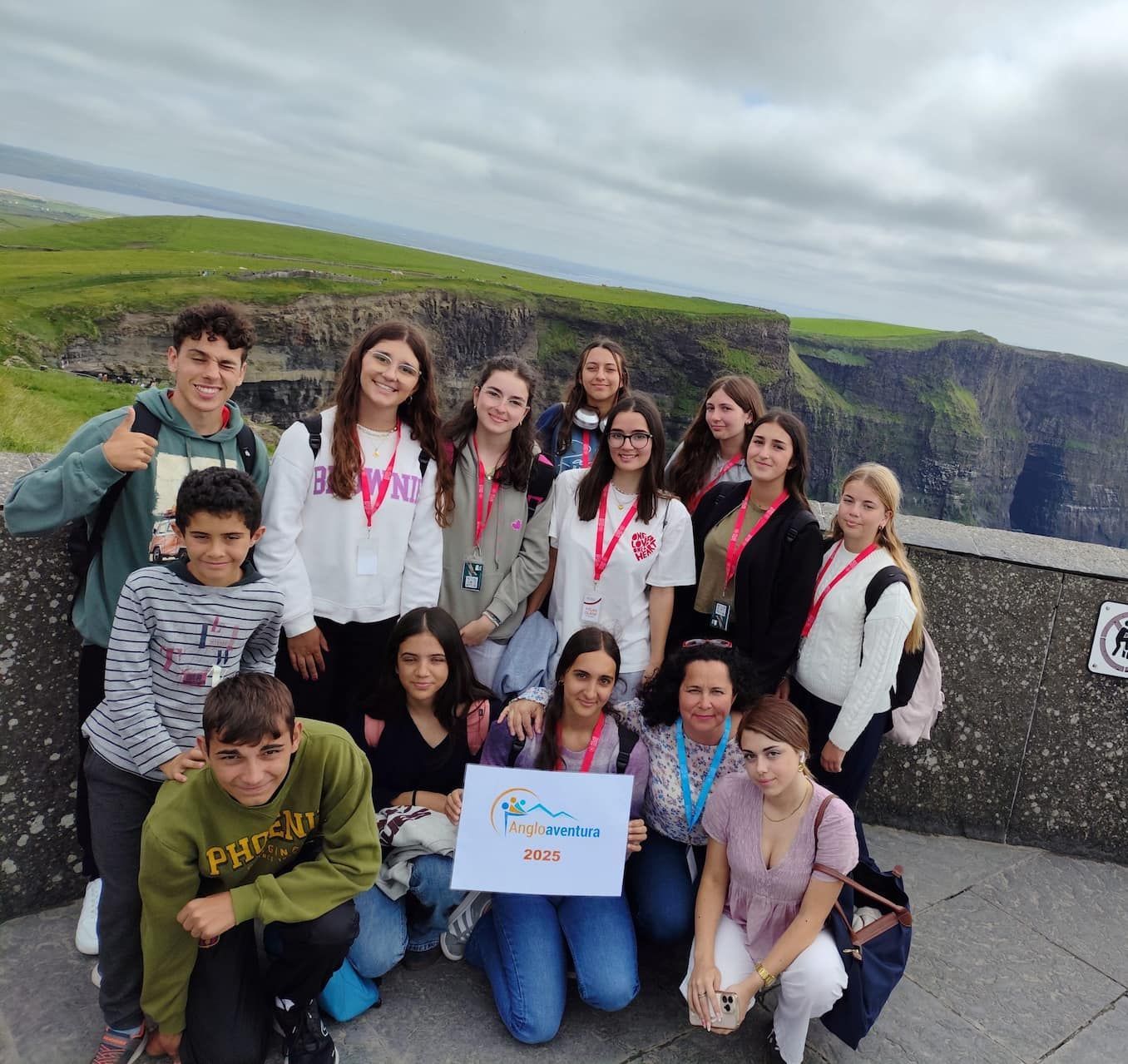 Un grupo de personas en un acantilado con vistas al océano. Llevan un cartel, sonríen y posan para una foto.