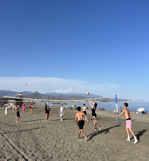 Gente jugando voleibol de playa en una orilla de arena bajo un cielo azul brillante.