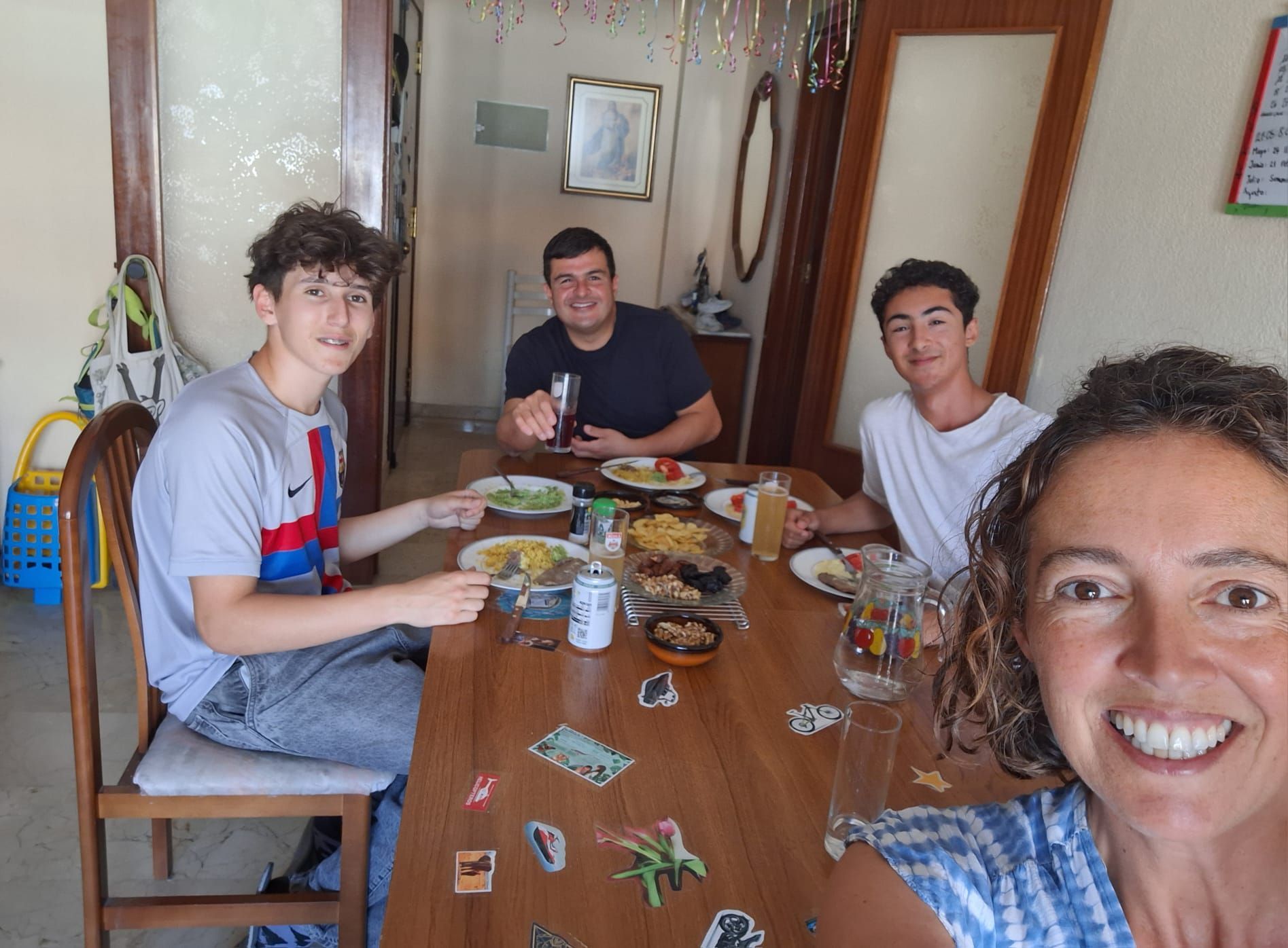 Una mujer se toma una selfi en una mesa con tres personas. Hay comida y bebidas sobre la mesa.
