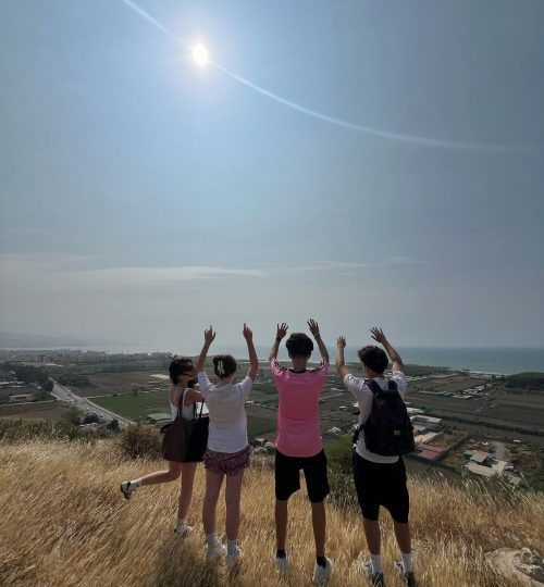 Cuatro personas en la cima de una colina con los brazos levantados hacia el sol brillante, con vistas a un paisaje.
