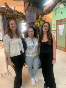 Tres personas posando frente a una exposición decorada, una mujer y dos mujeres jóvenes.
