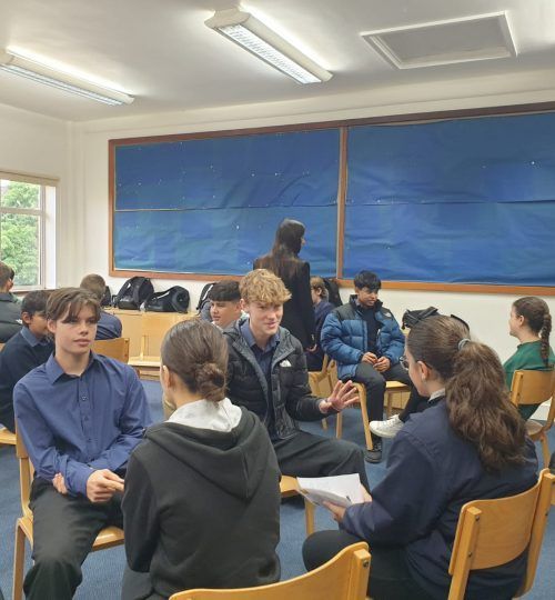 Los estudiantes en un aula, sentados en círculo, participan en una discusión.