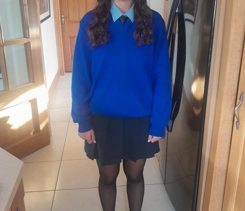 Persona con uniforme escolar: suéter azul, falda negra, camisa con cuello, corbata y medias.