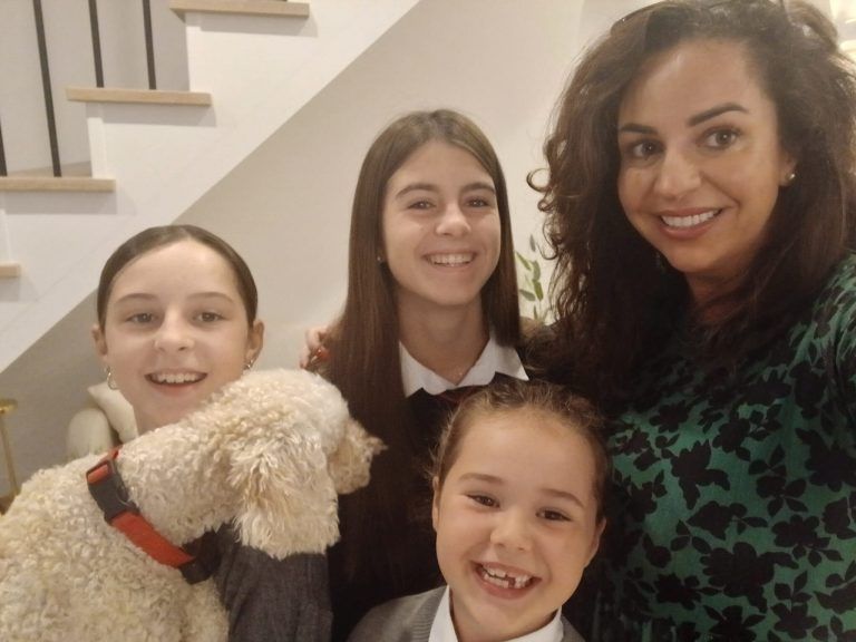 Familia de cuatro con un perro, sonriendo frente a las escaleras.