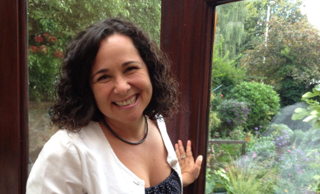 Grupo de personas colaborando alrededor de una mesa; banderas, ordenador portátil y papeles presentes.