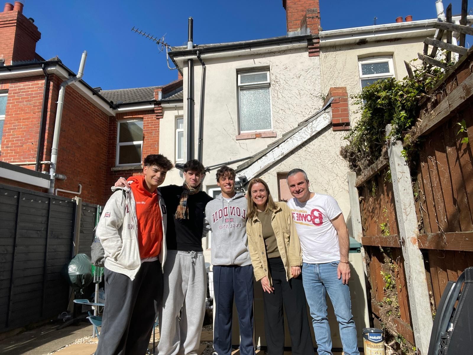Cinco personas posando al aire libre frente a una casa en un día soleado.