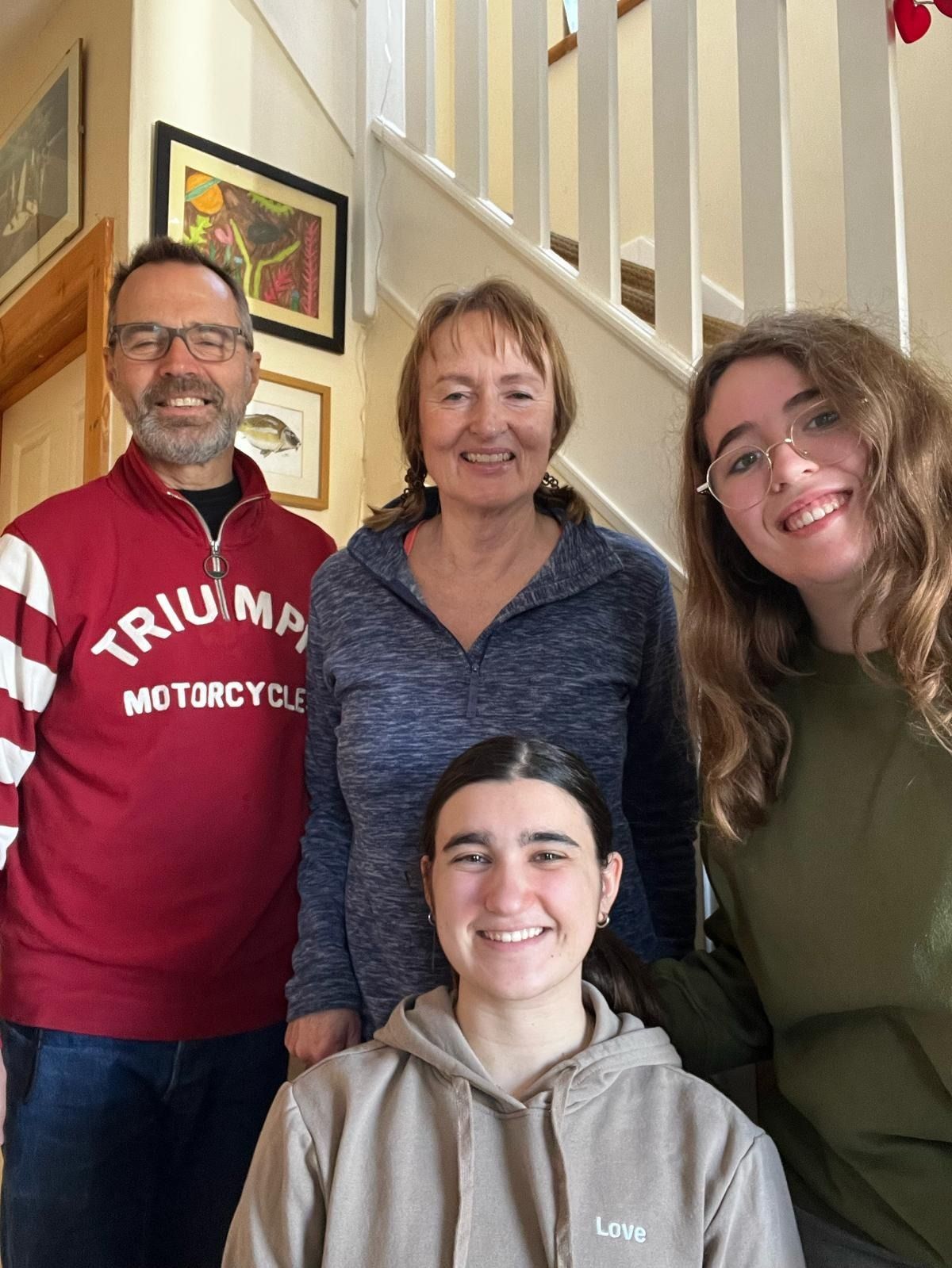 Retrato familiar: cuatro personas sonriendo, de pie frente a una escalera, una de ellas vistiendo una camiseta de Triumph.