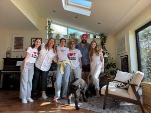 Grupo de personas y perros sonriendo en el interior cerca de ventanas, plantas y un piano.