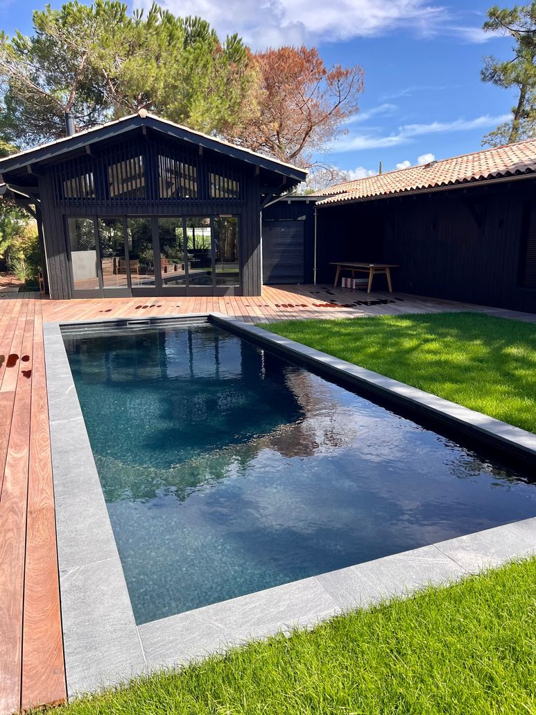 Lien vers la page Entretien de piscines Piscine rectangulaire dans un jardin, maison peinte en foncé, pelouse verte, briques rouges